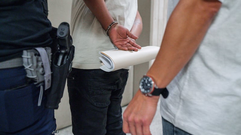 FILE - A man holds his immigration paperwork while handcuffed after being detained by...